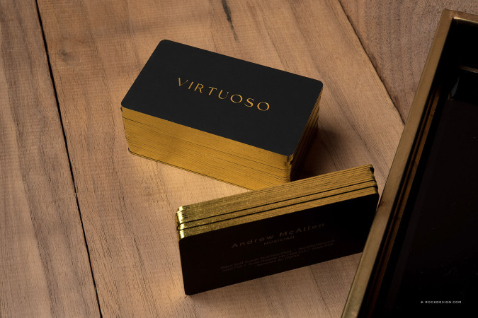 Black soft suede business cards with gold foil edges and metallic gold lettering, displayed on a wooden surface for a luxury business card design.