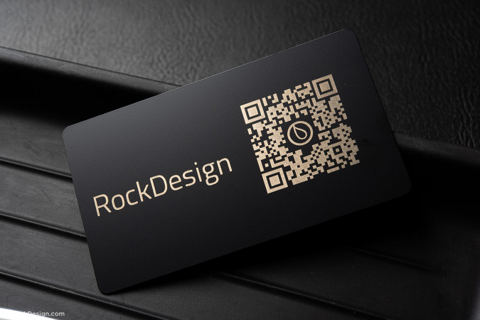 Luxurious black metal business card with gold-etched QR code and “RockDesign” branding, placed on a textured black surface.