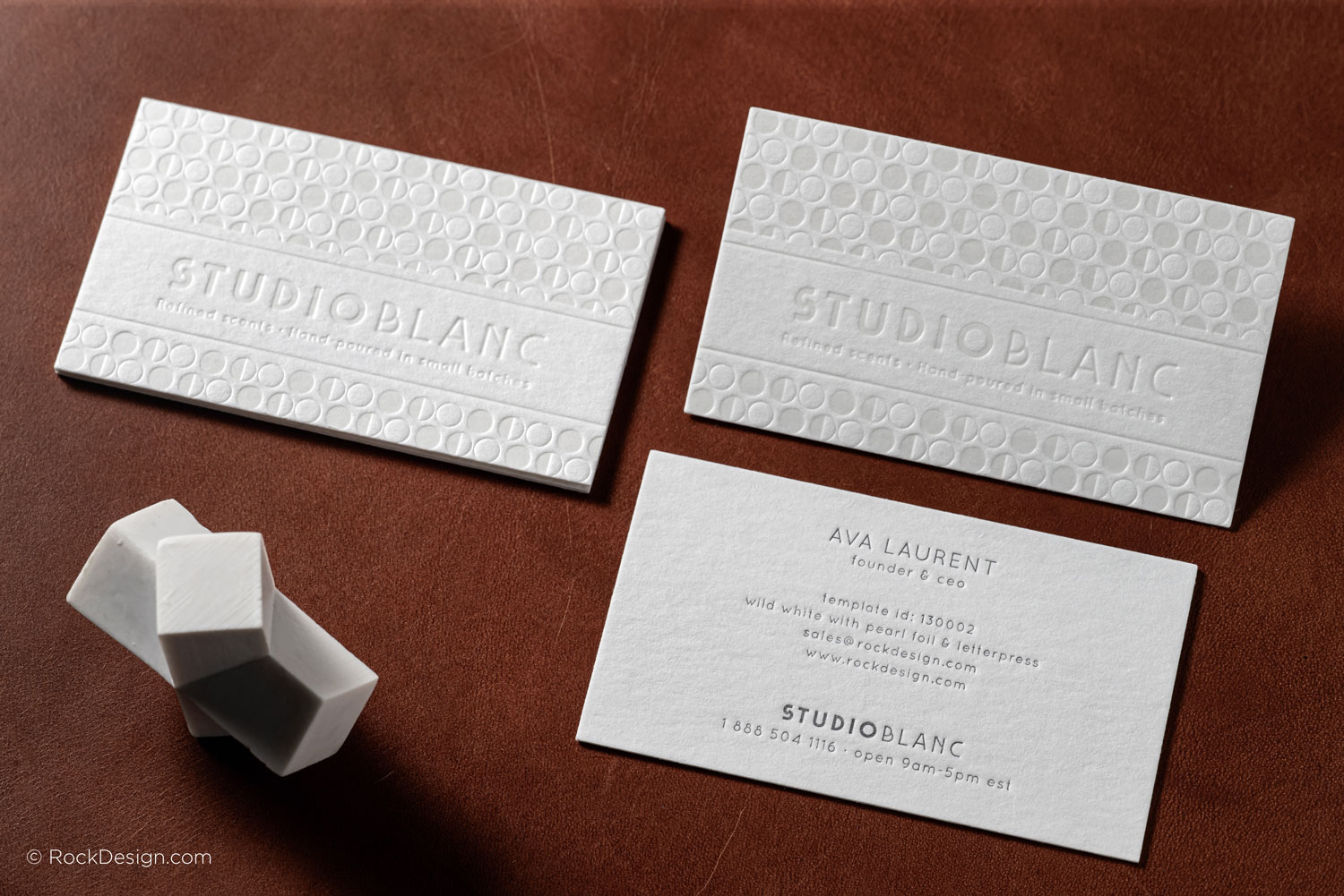 Luxury letterpress business cards on wild white cotton cardstock with pearl foil stamping and embossed pattern for Studio Blanc, photographed on a brown leather surface.